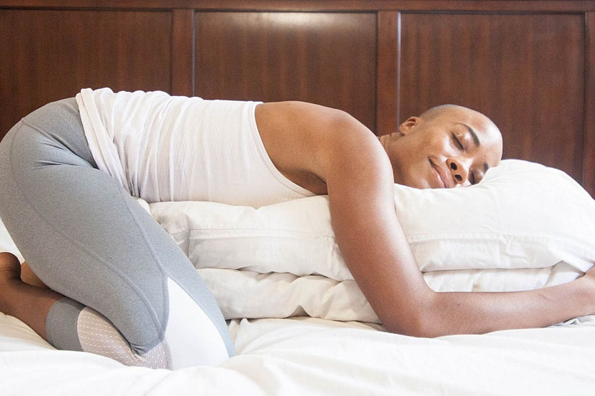 person laying on bed in child's pose with pillows as a prop underneath their body