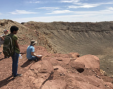 Ursinus students looking down over rim of a meteor crater during a Planetary Crater Consortium (PCC) field trip in August 2019.