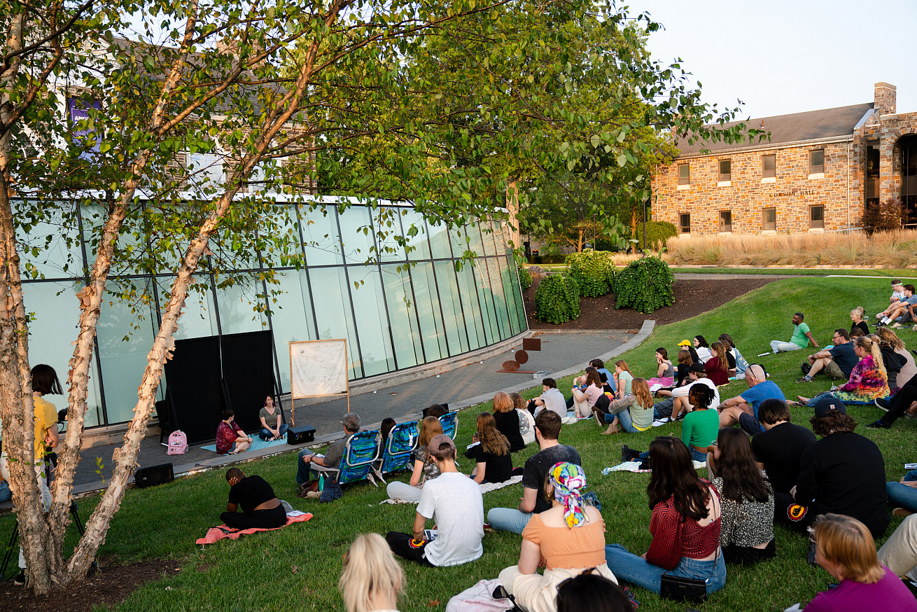 Students and members of the community are on the Berman lawn watching a play in the Berman Amphit...